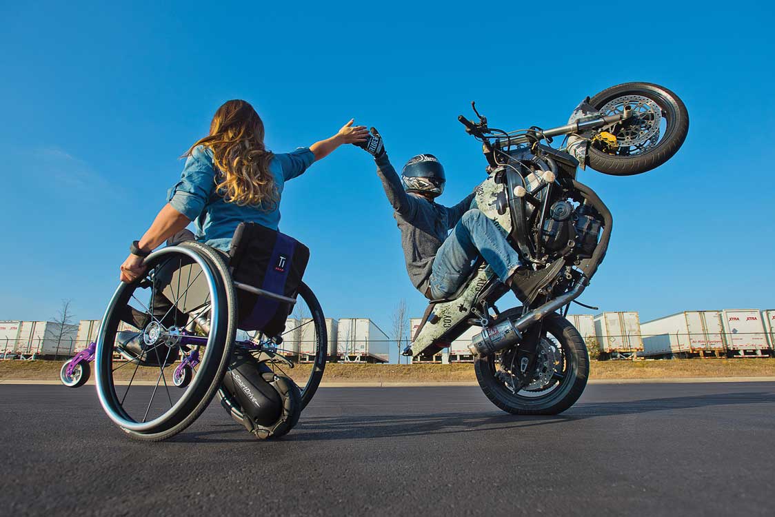 behind a wheelchair riding a wheelie and giving a motorcycle a